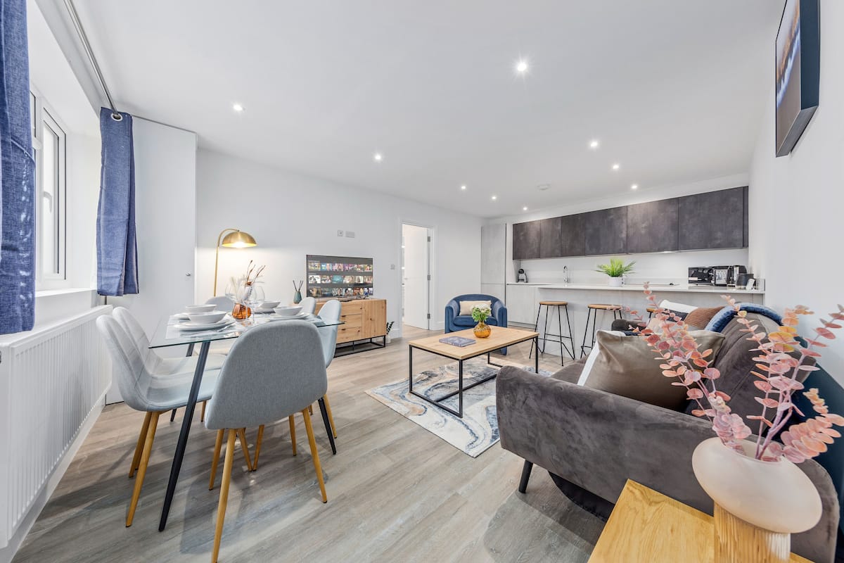 A modern living room with a dining area, a kitchen, and a view of the outdoors.