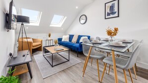 Ein modernes Wohnzimmer mit einer Couch, einem Couchtisch und einem Esstisch. Es gibt Dachfenster und eine Uhr an der Wand.