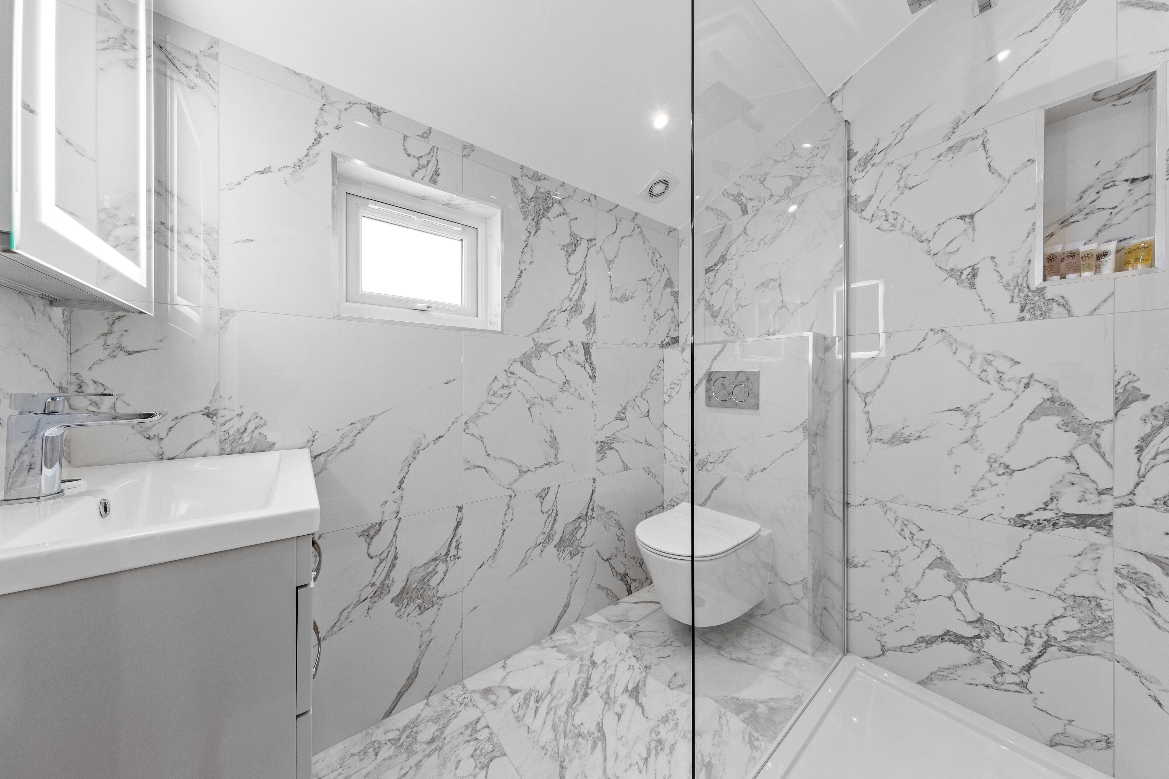 A bathroom with marble walls, a toilet, a sink, and a glass shower enclosure.
