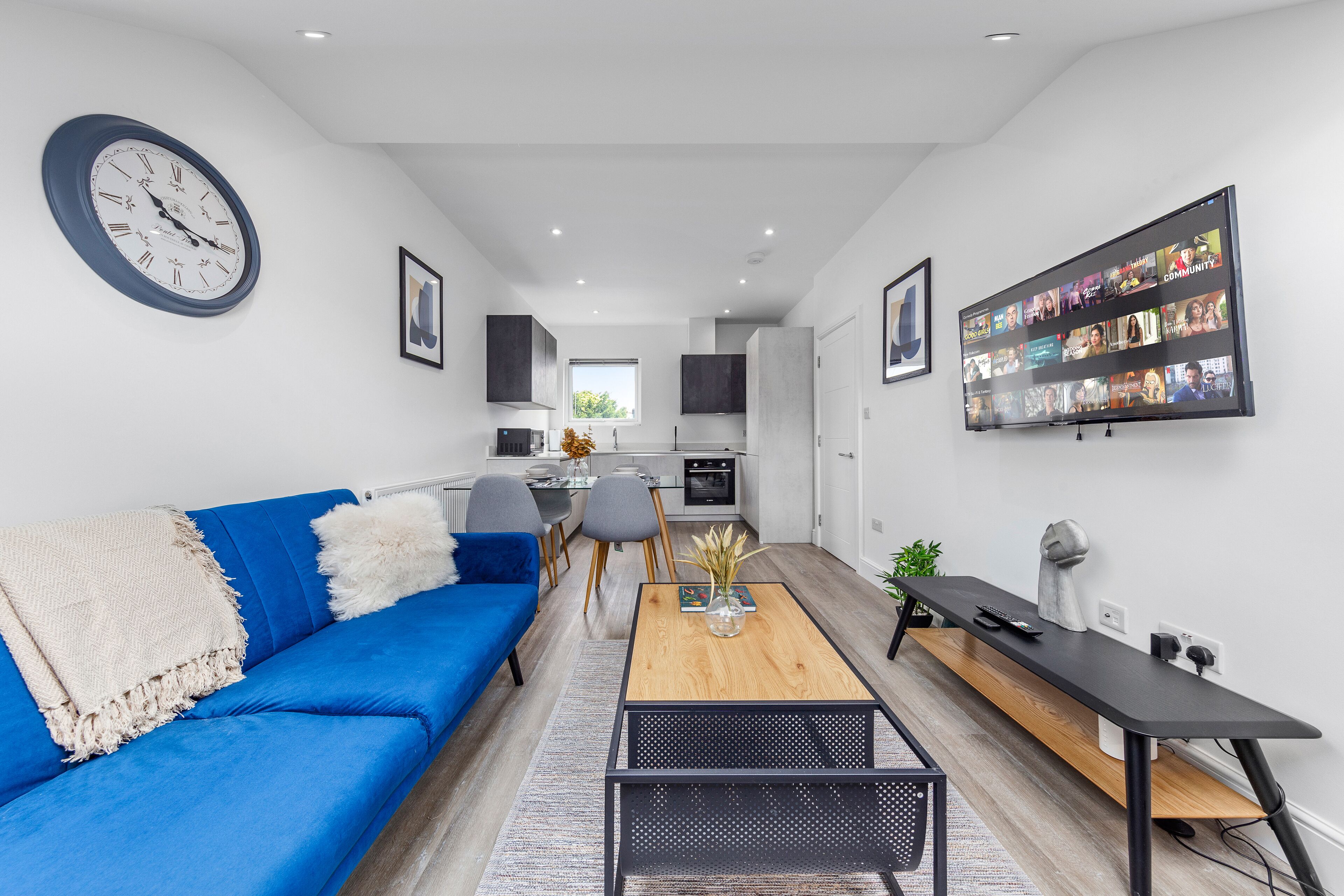 A modern living room with a blue sofa, a coffee table, and a flat-screen TV mounted on the wall.