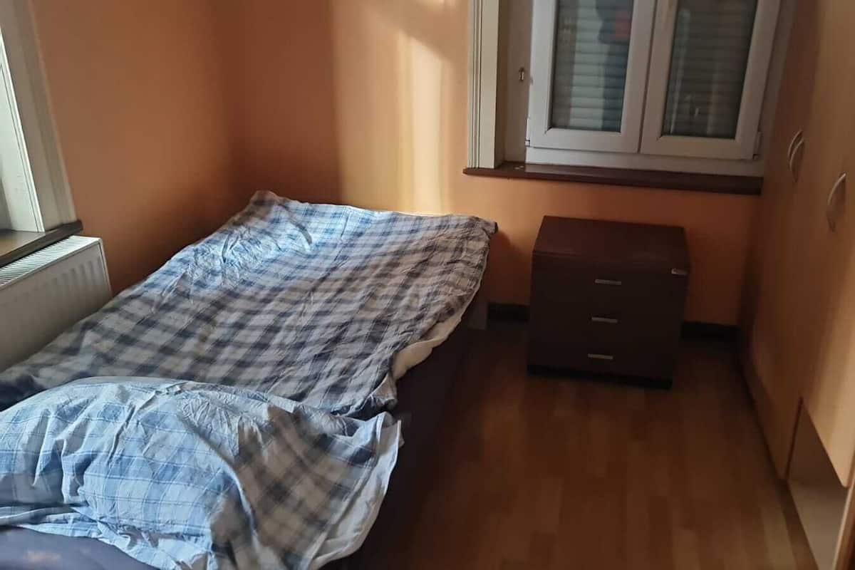 A small bedroom with a bed, a chest of drawers, and a window.