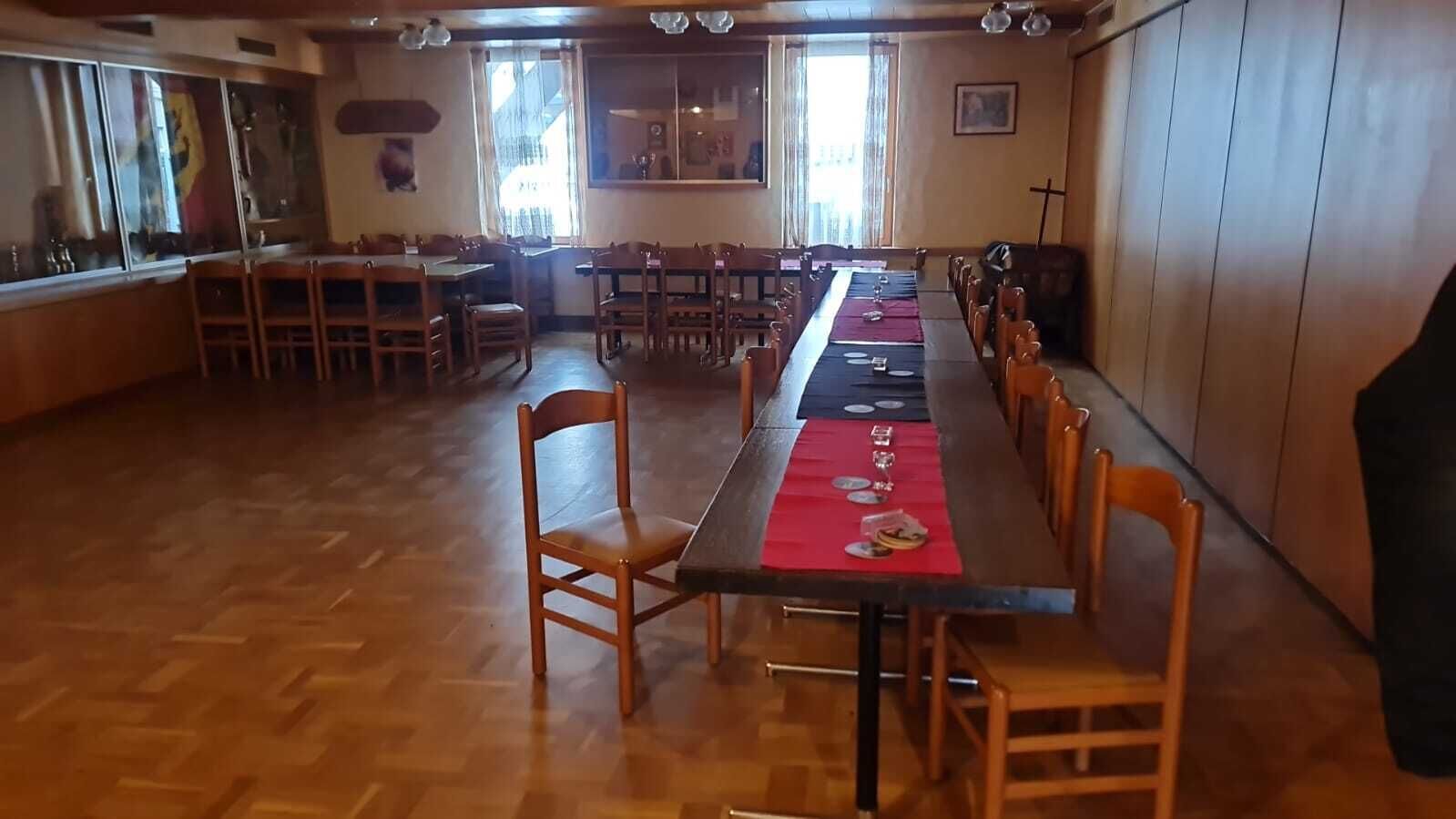 Ett långt matbord med stolar, ett trägolv och ett kors på väggen.