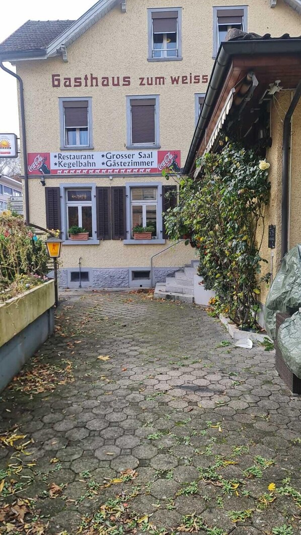 A building named "Gasthaus zum Weiss" with a Coca-Cola sign, a restaurant, and a larger room indicated by the sign.