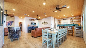 A spacious kitchen with wooden floors, a dining area with blue chairs, and ceiling fans. - Captain Twig by Avantstay Getaway 3 Blocks From Beach (Port Aransas)