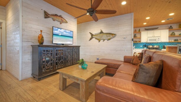 A cozy living room with a wooden ceiling, a leather sofa, a wooden coffee table, and a television. - Captain Twig by Avantstay Getaway 3 Blocks From Beach (Port Aransas)