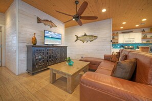 A cozy living room with a wooden ceiling, a leather sofa, a wooden coffee table, and a television. - Captain Twig by Avantstay Getaway 3 Blocks From Beach (Port Aransas)