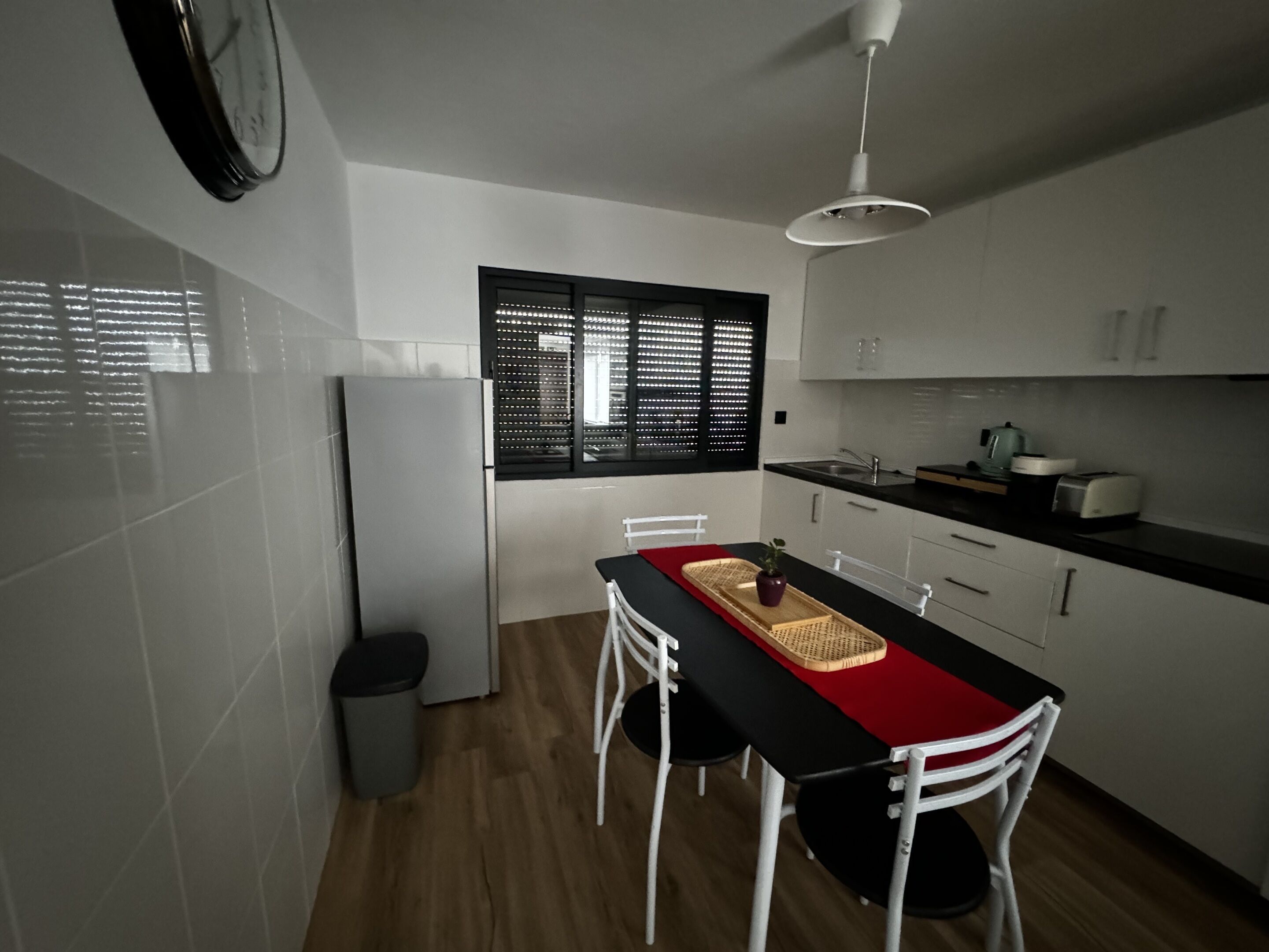 A compact kitchen with white cabinets, a black countertop, and a dining area with a red table runner.