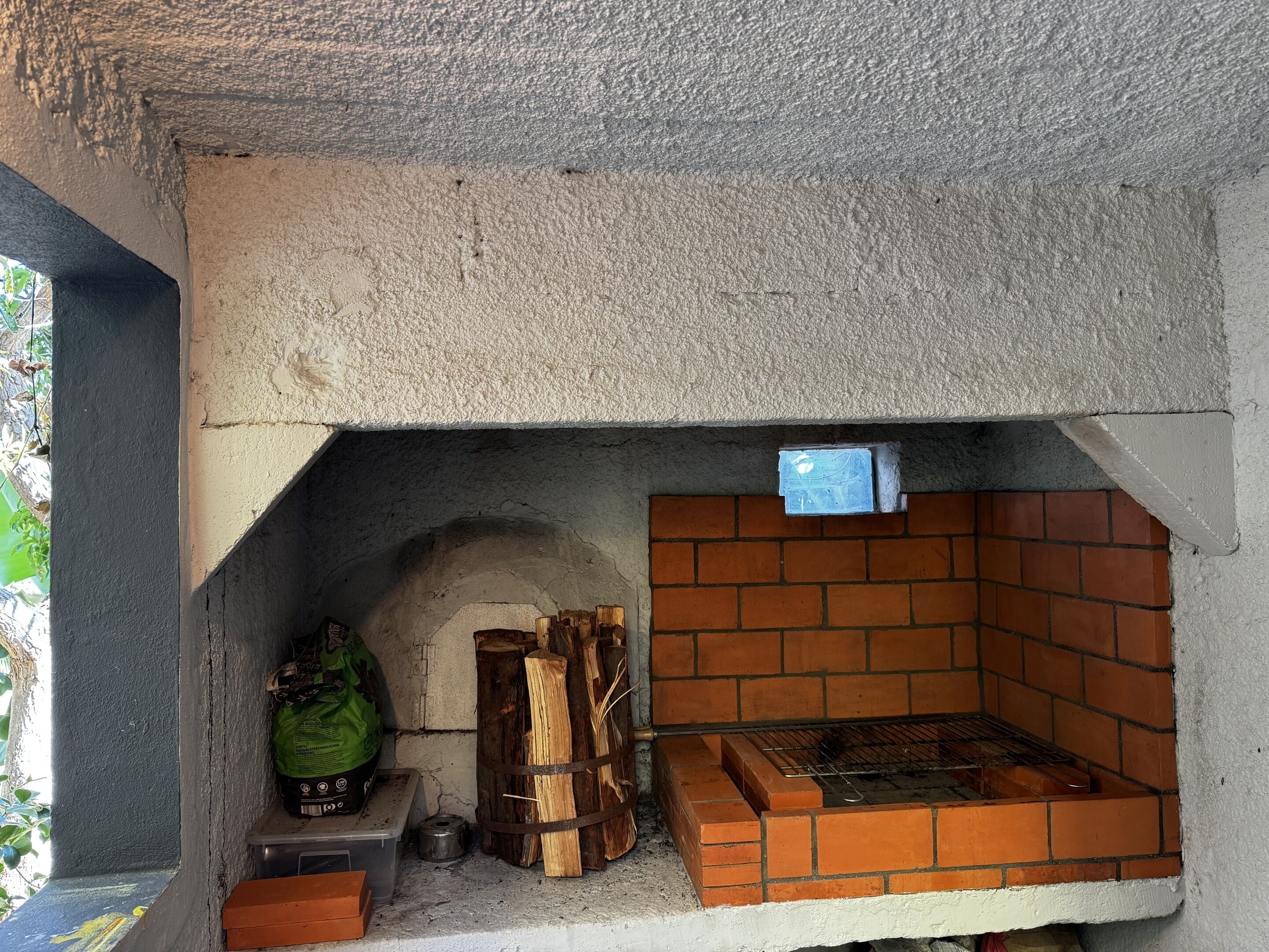 A brick oven with a metal rack, a green bag, and a small container on a table.