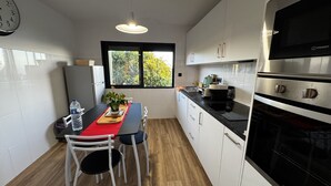 Cozinha moderna com armários brancos, bancada preta e forno de aço inoxidável. Há uma janela com vista para o verde lá fora.