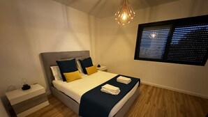Quarto moderno com cama, mesas de cabeceira, luminária decorativa e janela com vista para a cidade.