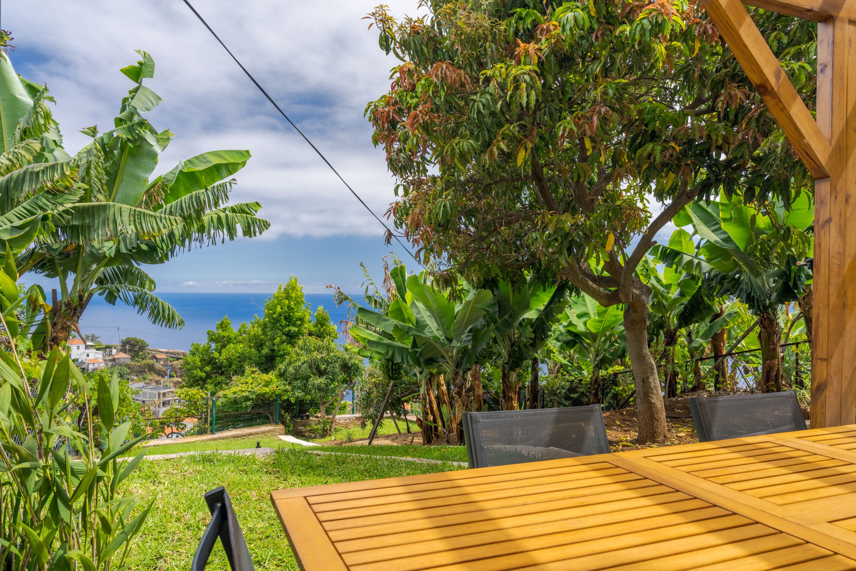 A wooden table with chairs in a garden area with a view of the sea and houses in the background.