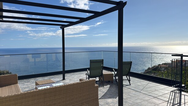 Varanda com móveis de vime e guarda-corpo de vidro com vista para o mar.