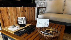 Uma mesa de centro de madeira com um controle remoto, um apoio para facas e uma cesta contendo um abridor de garrafa e outros utensílios.