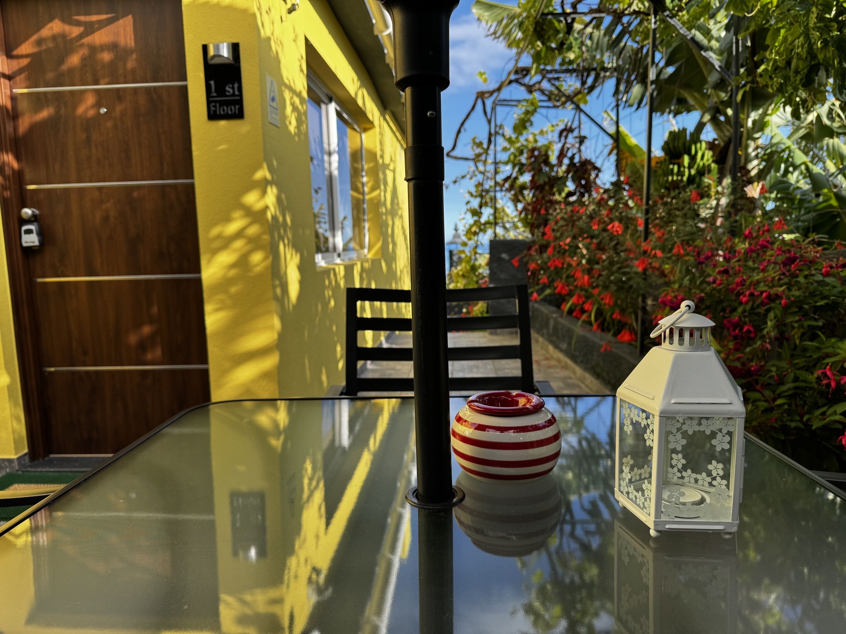 A glass table with a red and white striped bowl, a white lantern, and a black chair.