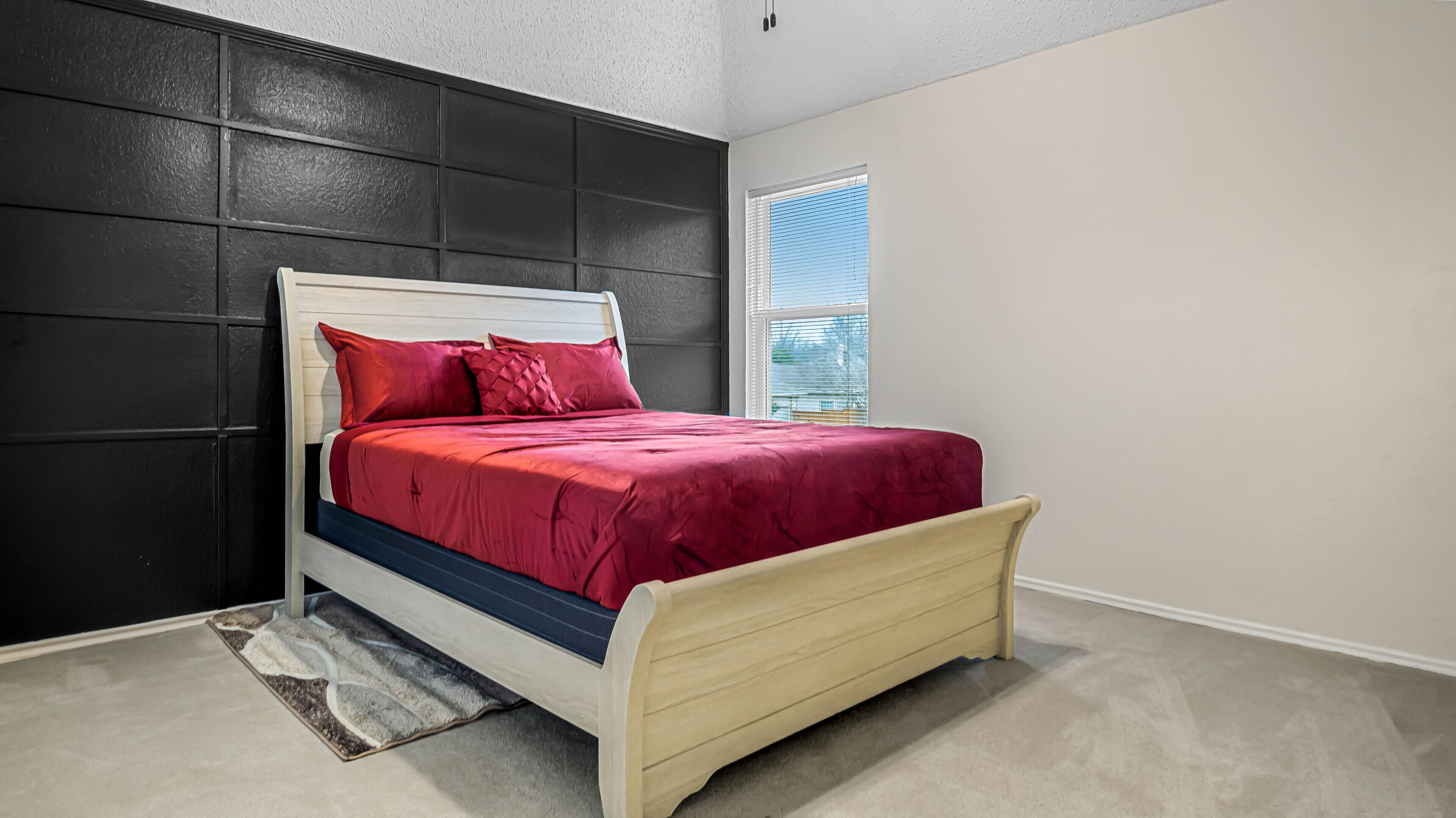 A bedroom with a bed, dark wall paneling, a window with blinds, and a carpet.