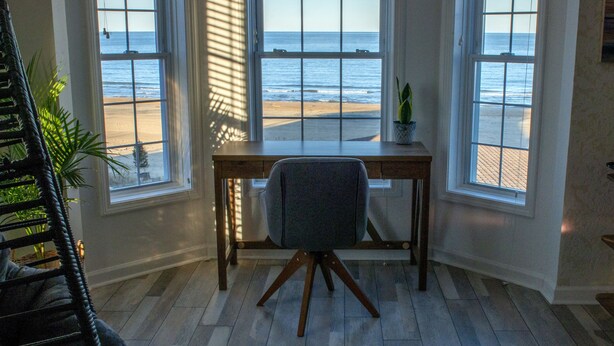 A room with a desk and chair, large windows with ocean views, and a potted plant on the windowsill. - Beachfront Getaway, pet friendly (Norfolk)