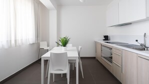 Eine moderne Küche mit weißen Schränken, einem Esstisch mit Stühlen, einem Blumentopf und einer Kaffeemaschine.