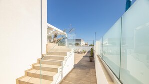 Un escalier moderne avec des rampes en verre menant à un balcon offrant une vue dégagée sur les environs.