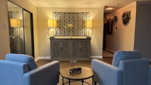 A living room with two blue armchairs, a small round table with a decorative item, and a patterned cabinet with two lamps. - Sylvia’s Getaway
 (Longview)