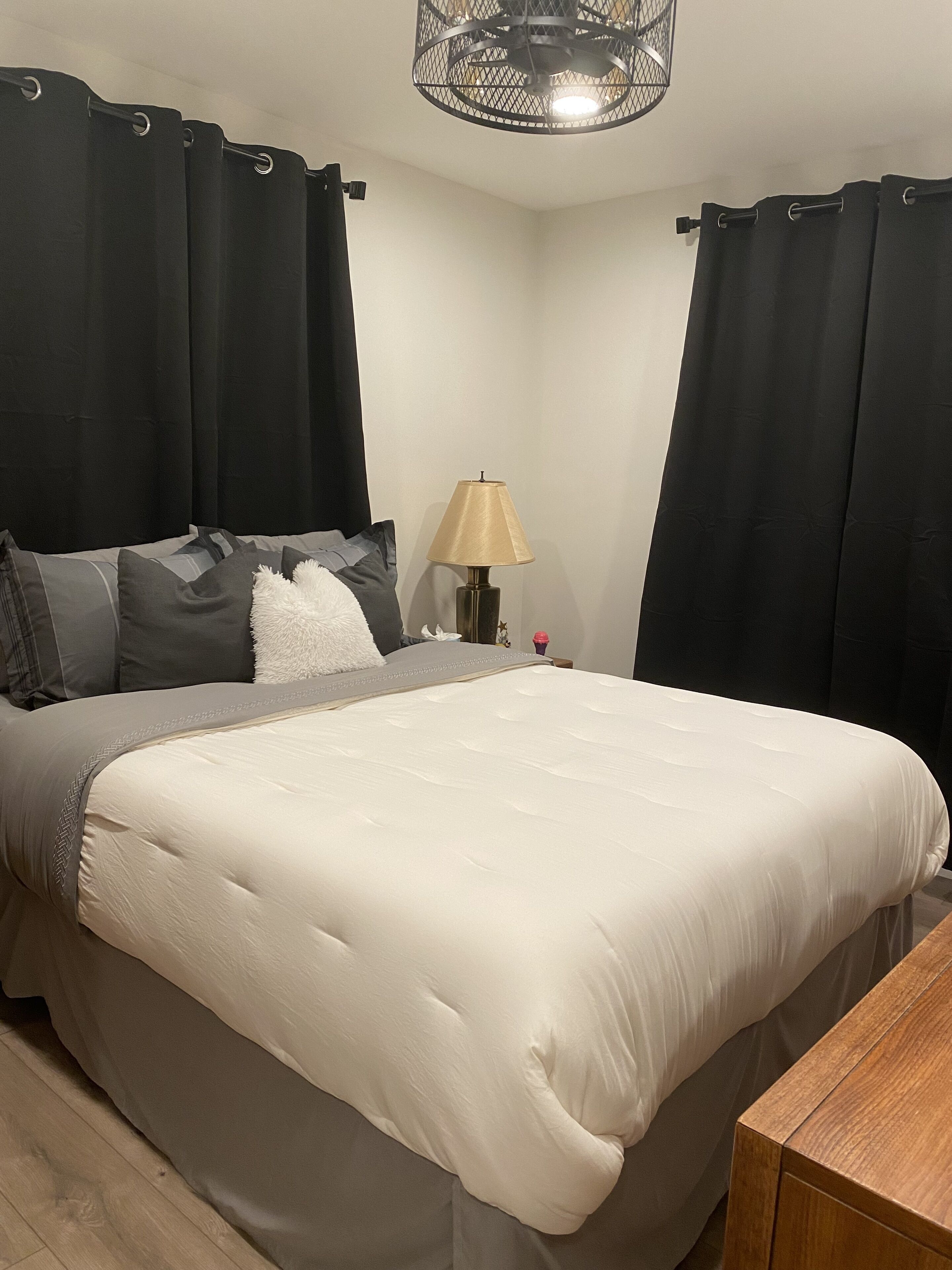 A bedroom with a bed, a nightstand, a lamp, and black curtains.