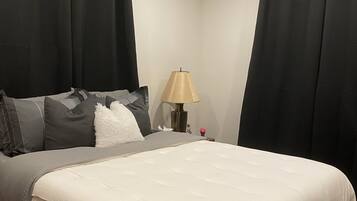A bedroom with a bed, a nightstand, a lamp, and black curtains.