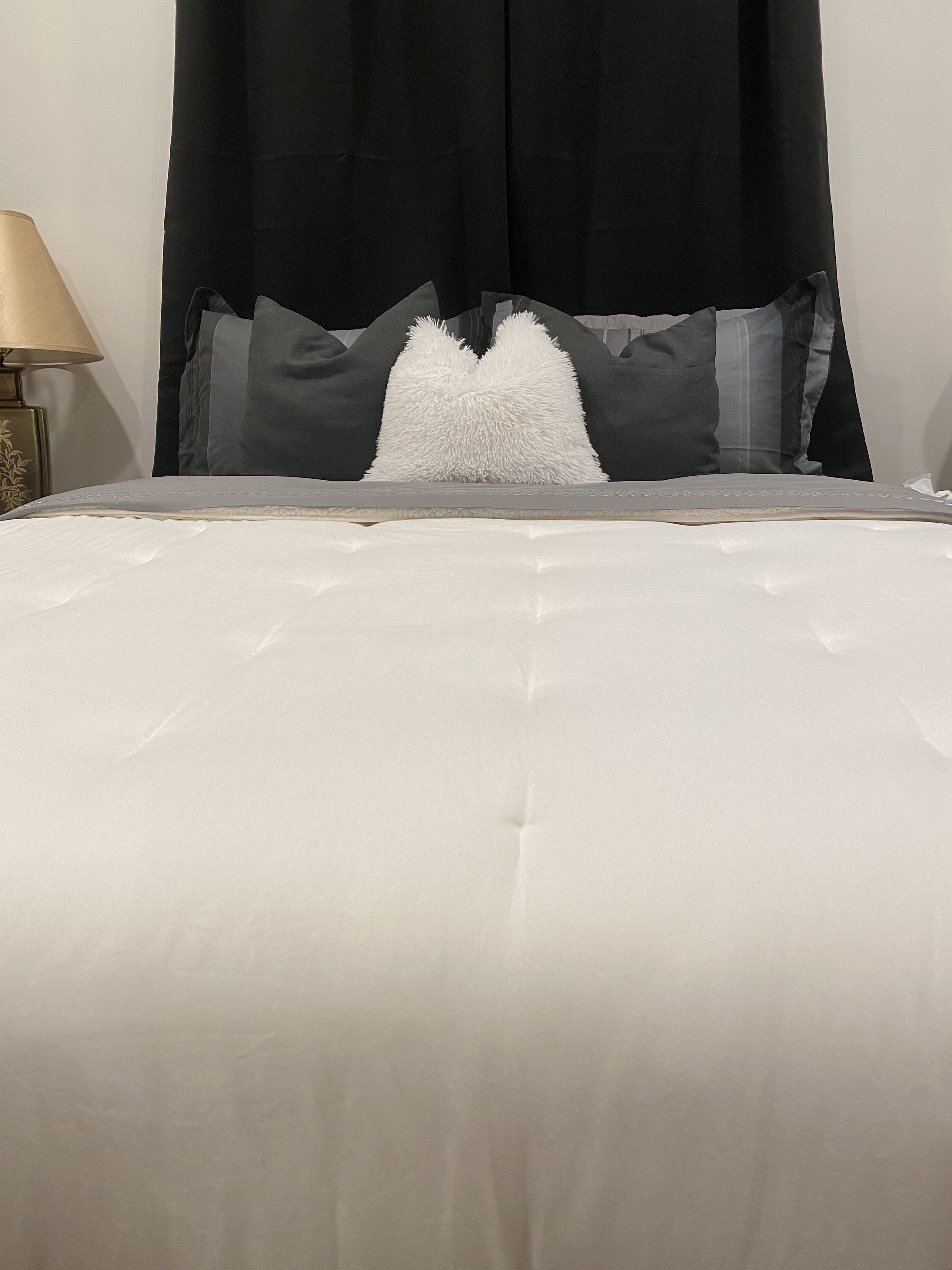 Cama com edredom branco, almofadas cinzas e cabeceira preta.