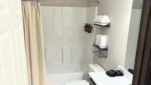 A modern bathroom with a shower, toilet, and sink. There are toiletries on a shelf and a towel rack.