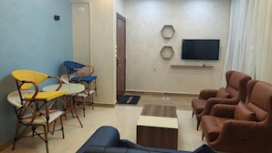 Una sala de estar con un sofá, sillas, una mesa de centro, un televisor y una puerta.