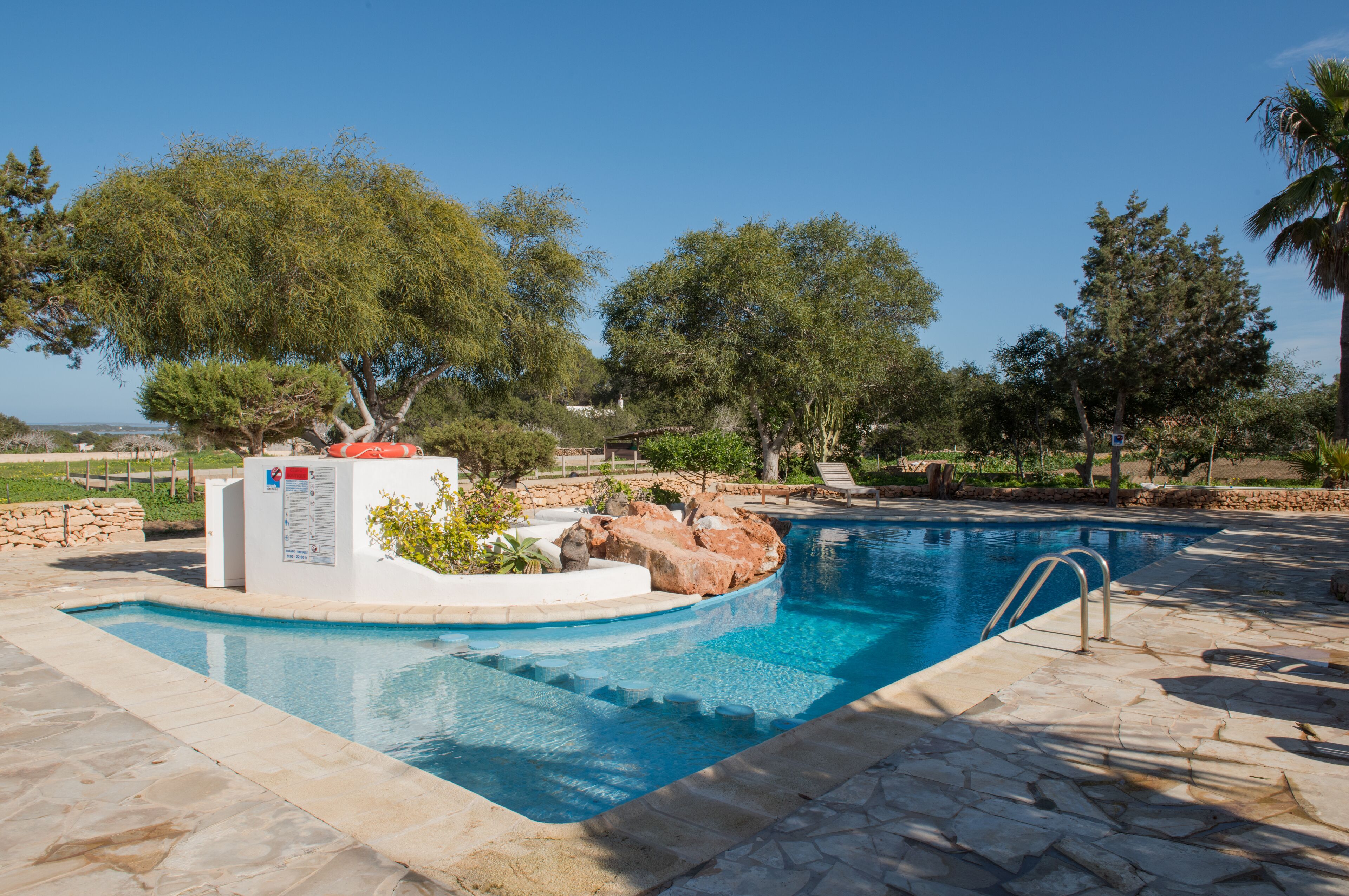 A swimming pool with a stone deck, surrounded by trees and a stone wall.