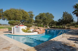 A swimming pool with a stone deck, surrounded by trees and a stone wall.