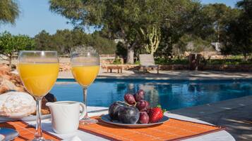 A table with breakfast items including croissants, a jug, and a plate with fruits by a poolside.