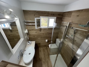 A modern bathroom with a wooden floor, a glass shower enclosure, a white sink, and a mirror.