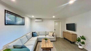 Ein modernes Wohnzimmer mit einem Ecksofa, einem Couchtisch aus Holz, einem Fernseher auf einem Holzboden und einem Topfpflanzen.