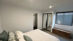 Ein Schlafzimmer mit Bett, Bank, Spiegel und Fenster mit Jalousien.