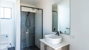 Ein modernes Badezimmer mit Duschkabine aus Glas, einem weißen Waschbecken und einem großen Spiegel.