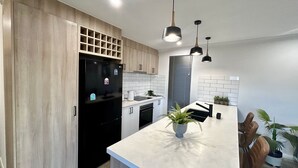 Eine moderne Küche mit Holzschränken, einem schwarzen Kühlschrank, einer weißen Arbeitsplatte und Pendelleuchten.