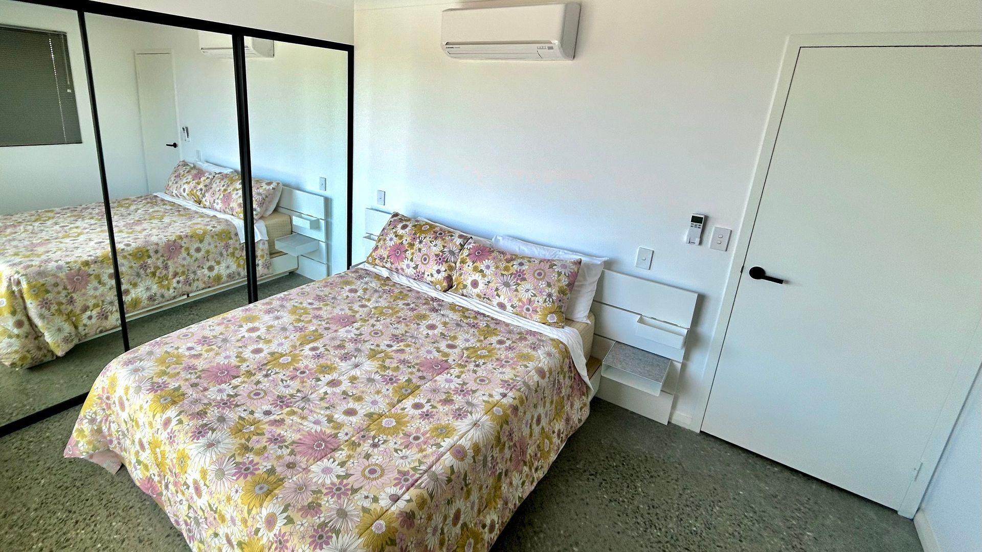 A bedroom with two beds, a wardrobe, a mirror, and a wall-mounted air conditioner.