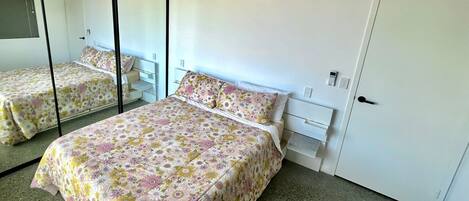 A bedroom with two beds, a wardrobe, a mirror, and a wall-mounted air conditioner.