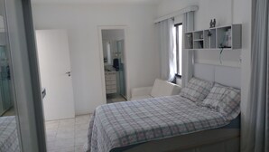 Ein Schlafzimmer mit Bett, Kommode und Spiegel. Eine Tür führt in einen anderen Raum.