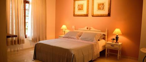 A bedroom with a bed, two bedside tables with lamps, a chair, and two framed pictures on the wall.