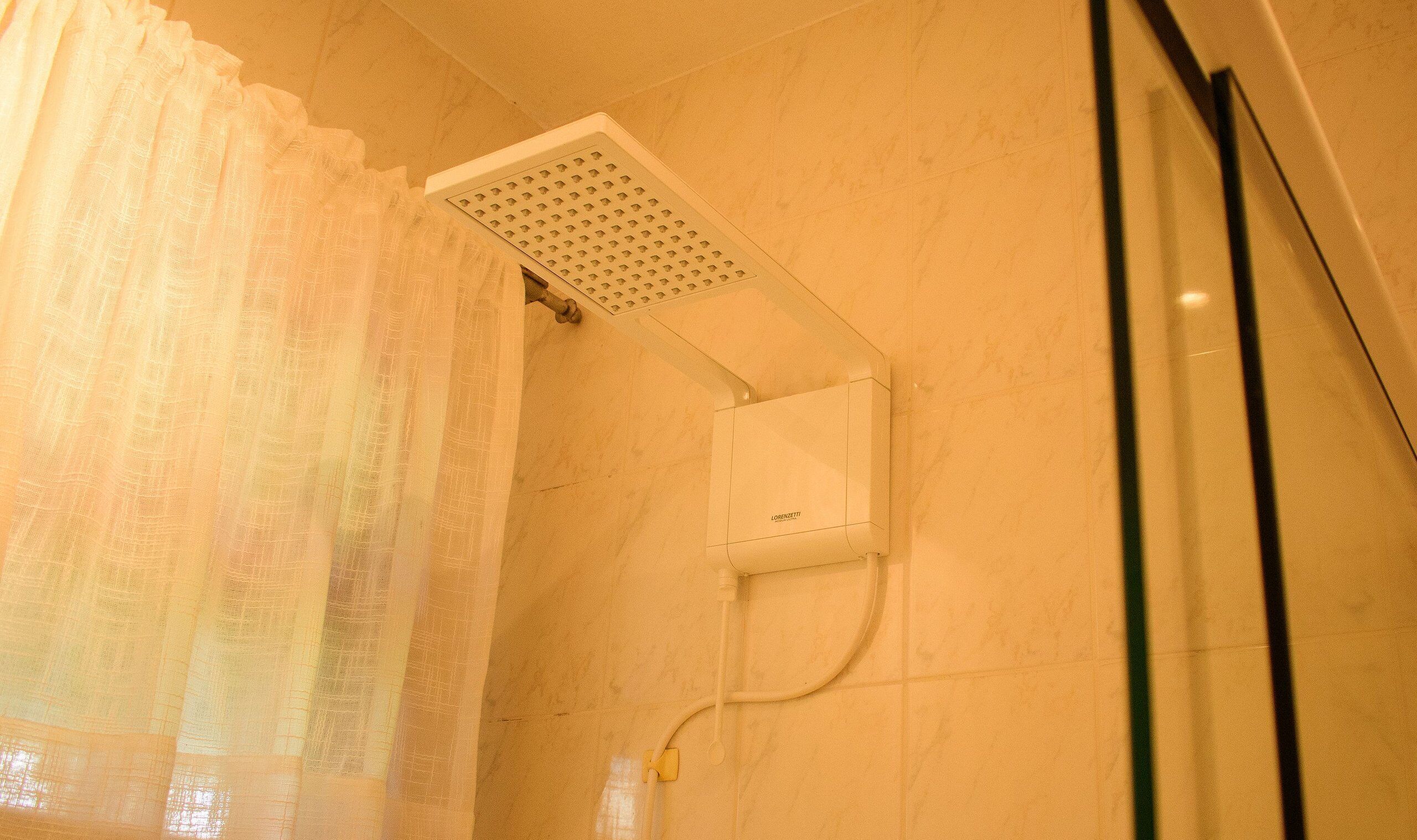 A shower with a ceiling-mounted rain showerhead, a control panel, and a curtain.