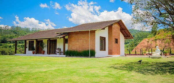 A two-story house with a tiled roof, a covered porch, and a garden with a Buddha statue.