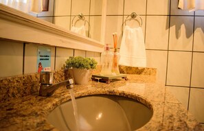 A bathroom with a granite countertop, a sink with running water, a potted plant, and a mirror above the mirror.