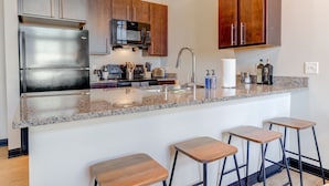 Una cocina moderna con electrodomésticos de acero inoxidable, armarios de madera, encimera de granito y taburetes de bar.