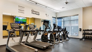 Un gimnasio con cintas de correr, bicicletas estáticas y una pantalla de televisión que muestra una escena natural.