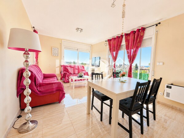 A modern living room with a dining area, a TV, and a view of the city.