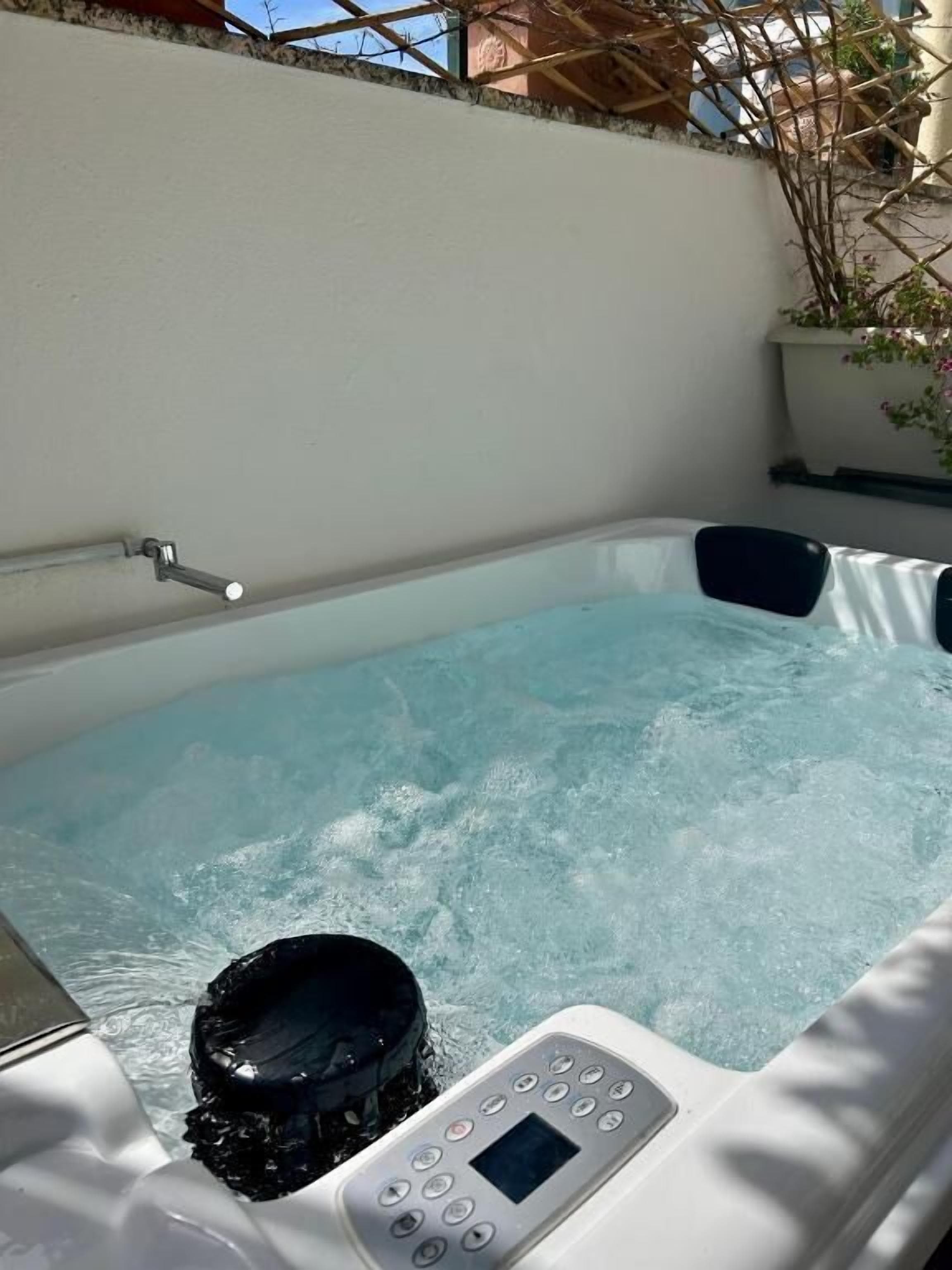 Ein Whirlpool mit Bedienfeld, umgeben von einer weißen Wand und einem Blumentopf.