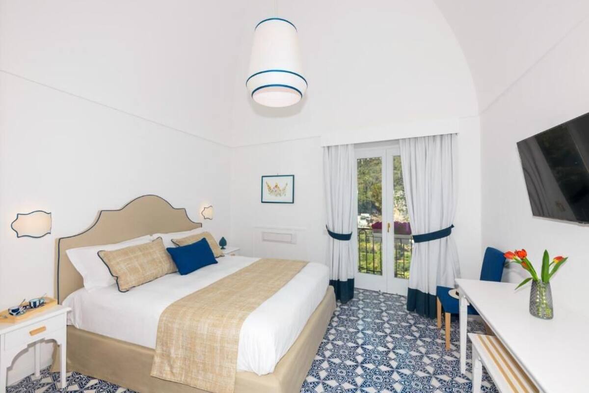A hotel room with a bed, bedside table, and a window with curtains.