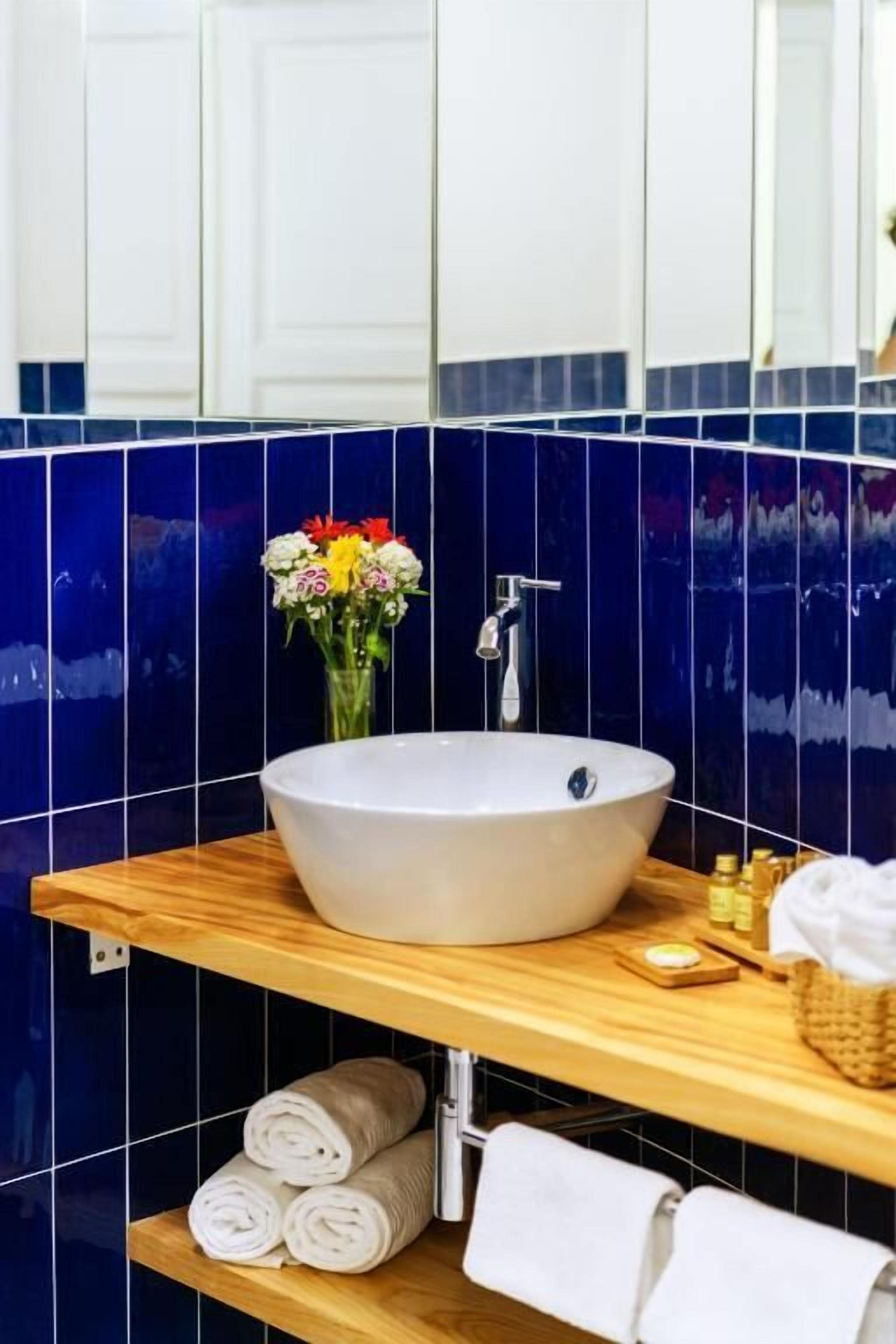 Ett badrum med ett stort, vitt handfat, en spegel och en hylla i trä med handdukar och hygienartiklar.