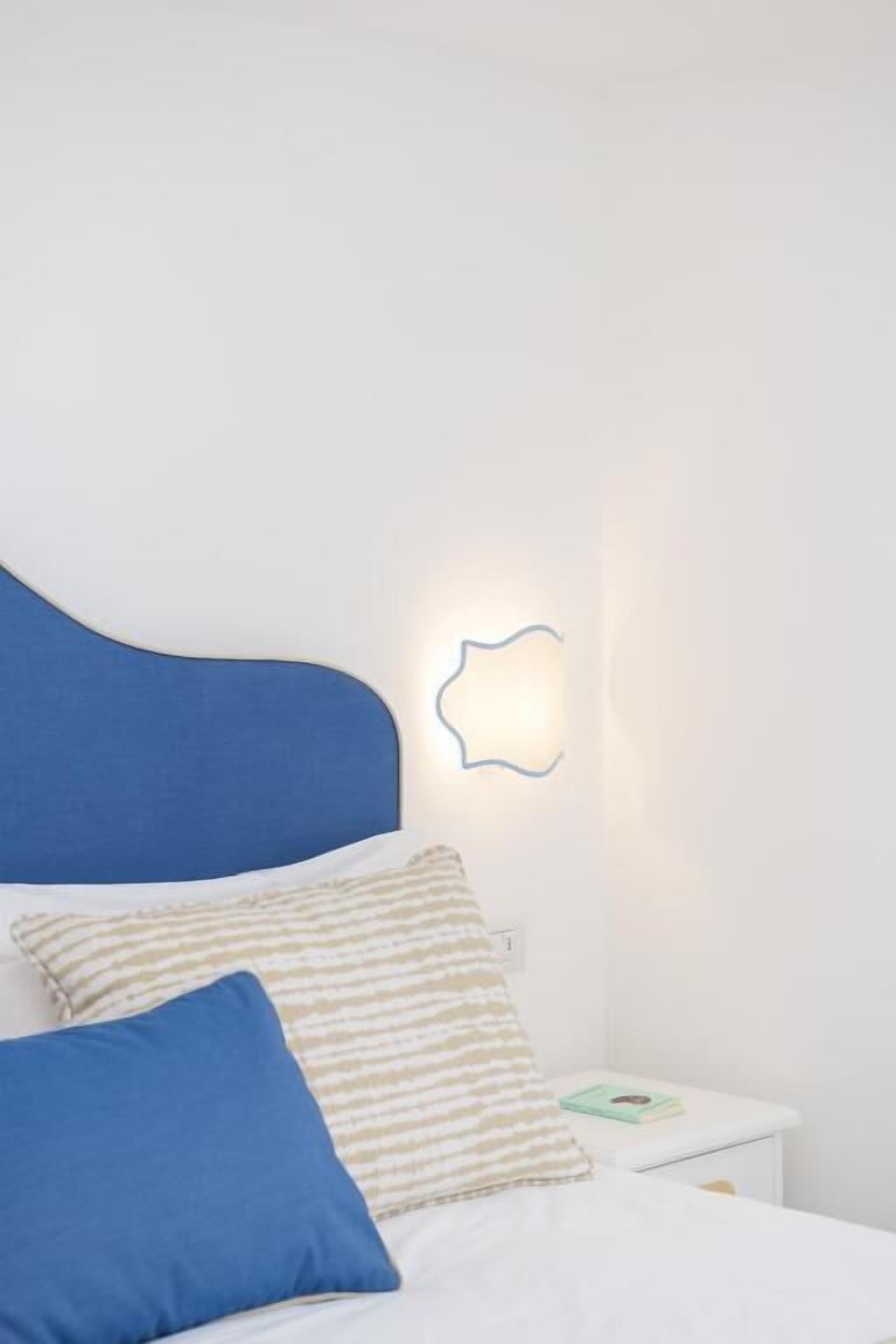 Une chambre à coucher avec un lit, des oreillers, une table de chevet et un luminaire fixé au mur.